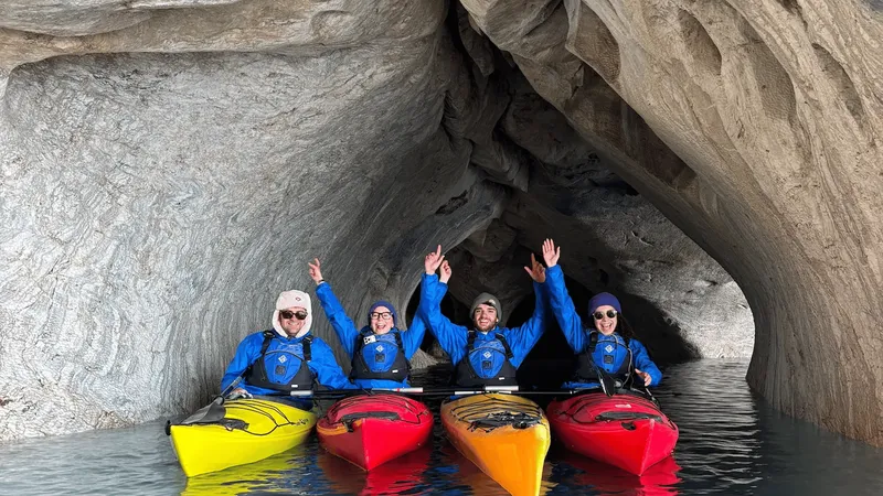 Guided kayak group in wetsuits approaching the marble caves Chile formations across turquoise Lake General Carrera water